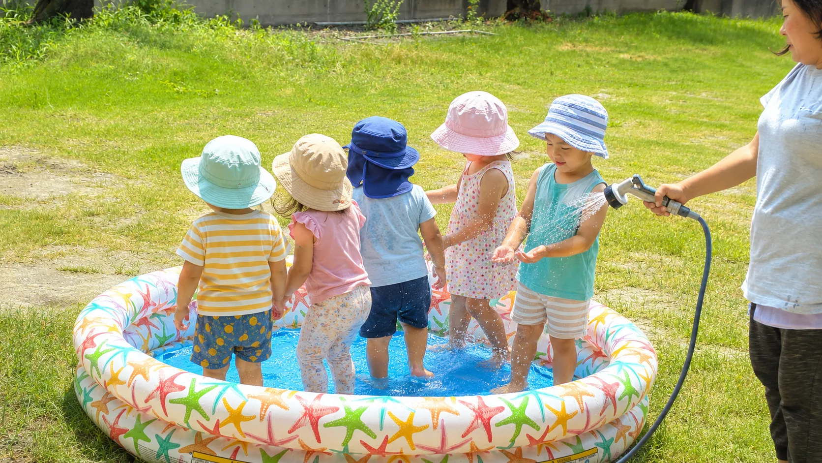 夏の園庭でプールと水遊びを楽しむ子どもたち