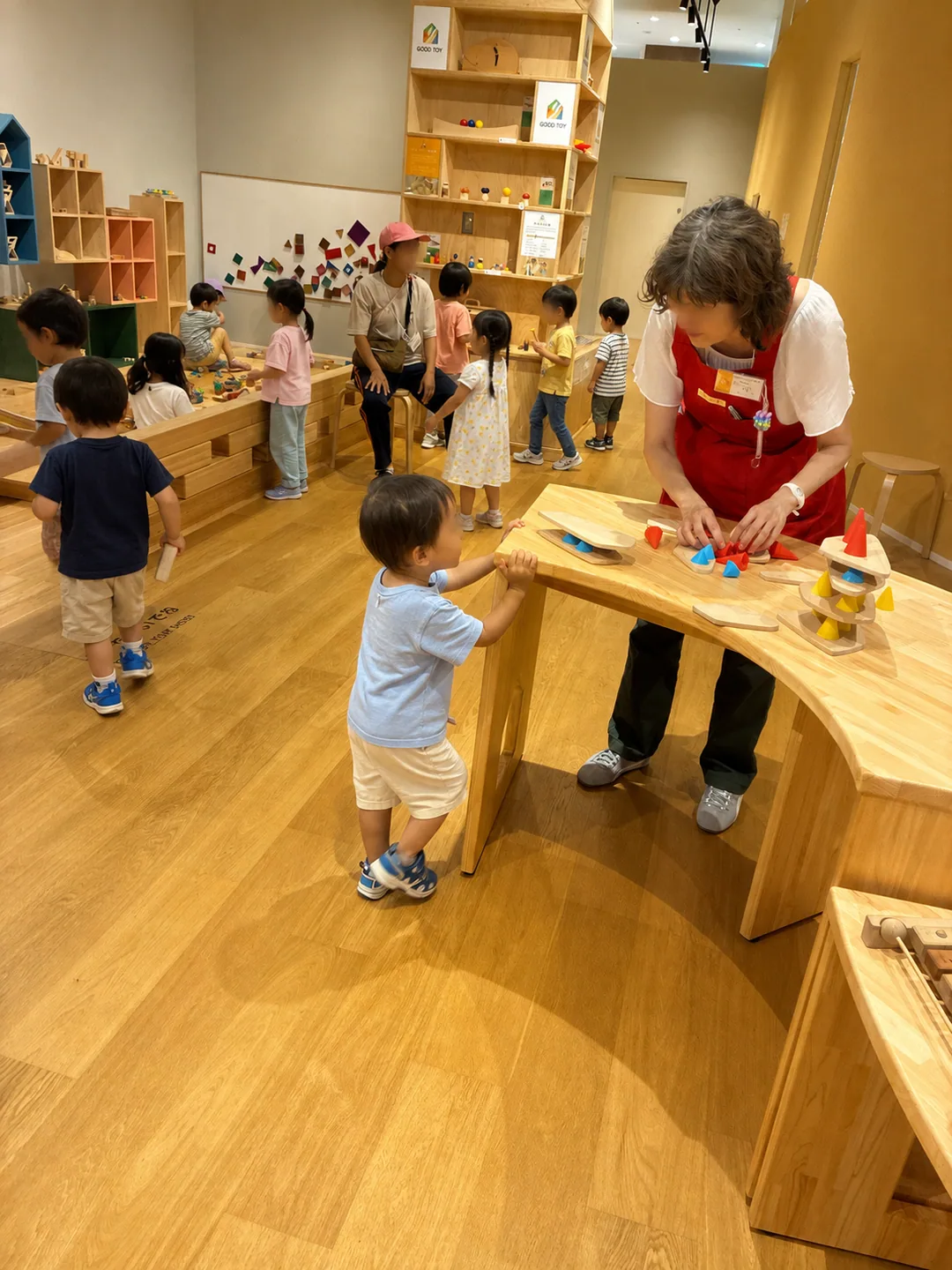 木のおもちゃが並ぶ館内でスタッフと遊ぶ子どもたち
